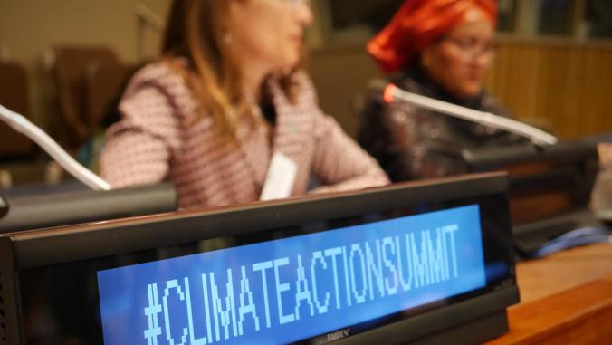 标志写着“# ClimateActionSummit。”背景为智利环境部长卡罗莱娜·施密特和联合国副秘书长阿米娜·穆罕默德。