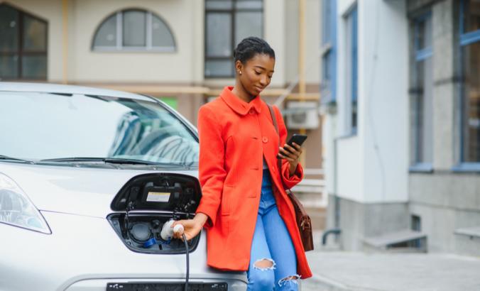 Black person standing in front of an electric car that is charging