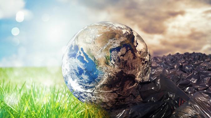 Globe on top of grass with sunny background on left side, on top of plastic trash bags and dark clouds on left side