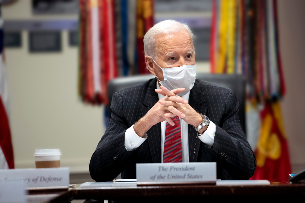 Joe Biden总统在会议上发表讲话。他戴着面具，双手折叠